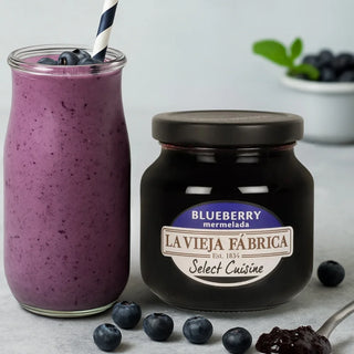 Jar of La Vieja Fábrica blueberry marmelade with a purple smoothie and blueberries on a light background